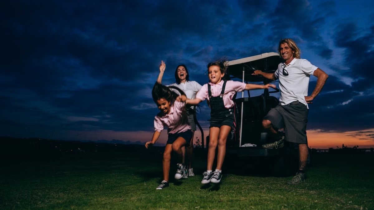 A family enjoying a fun golf outing with kids playing and adults smiling at sunset.